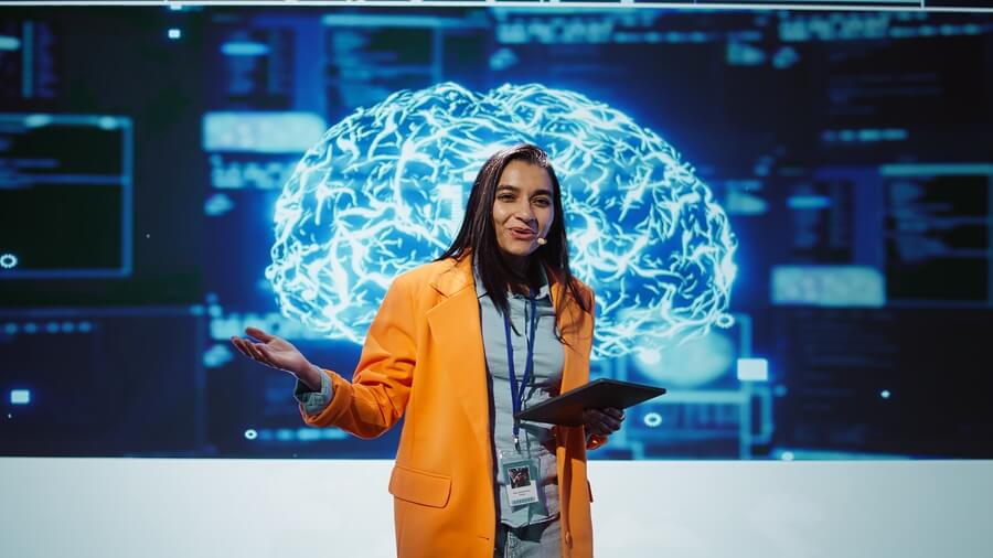 Que es inteligencia de negocios conclusiones - Mujer profesional con tableta en mano, explicando conceptos de inteligencia artificial frente a una pantalla con un cerebro digital iluminado y gráficos tecnológicos.